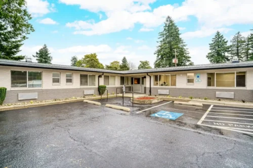 Modern courtyard featuring gray-clad buildings, spacious concrete pathway, and a planter with greenery under a bright sky.